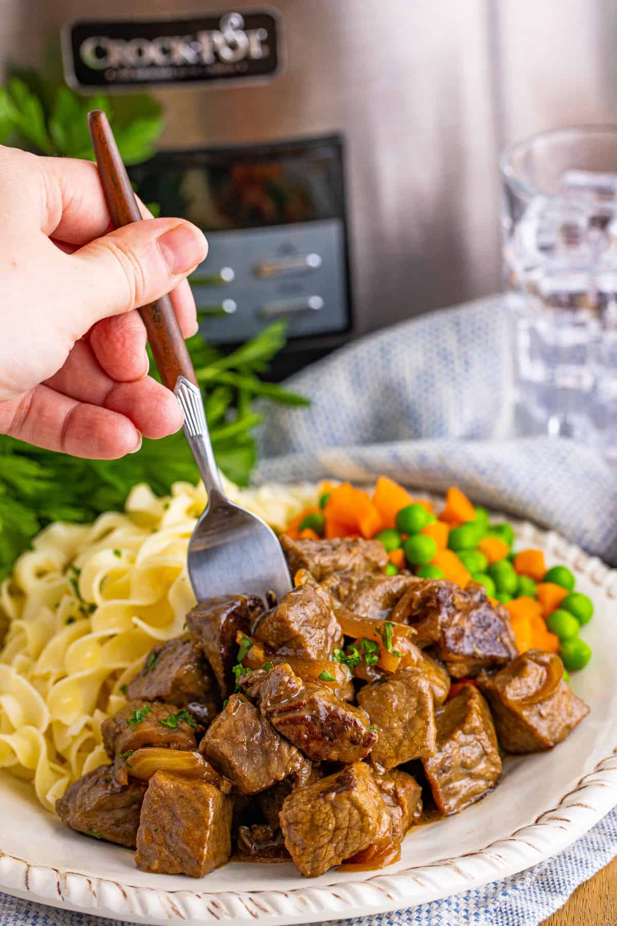 Hand with fork reaching in to take a crockpot steak bite off of plate.