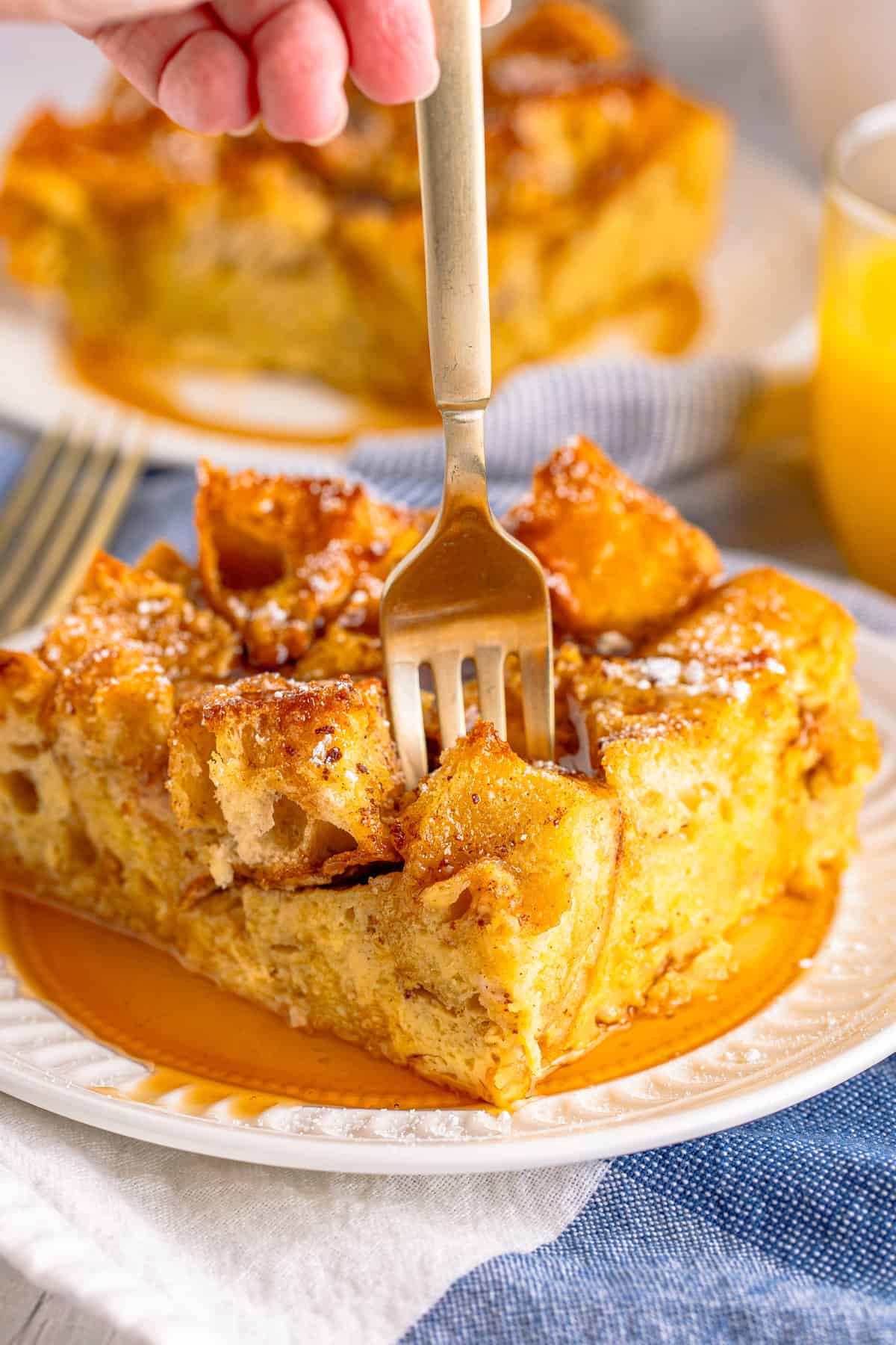 Fork digging into a piece of golden brown maple-syrup drenched French Toast casserole.
