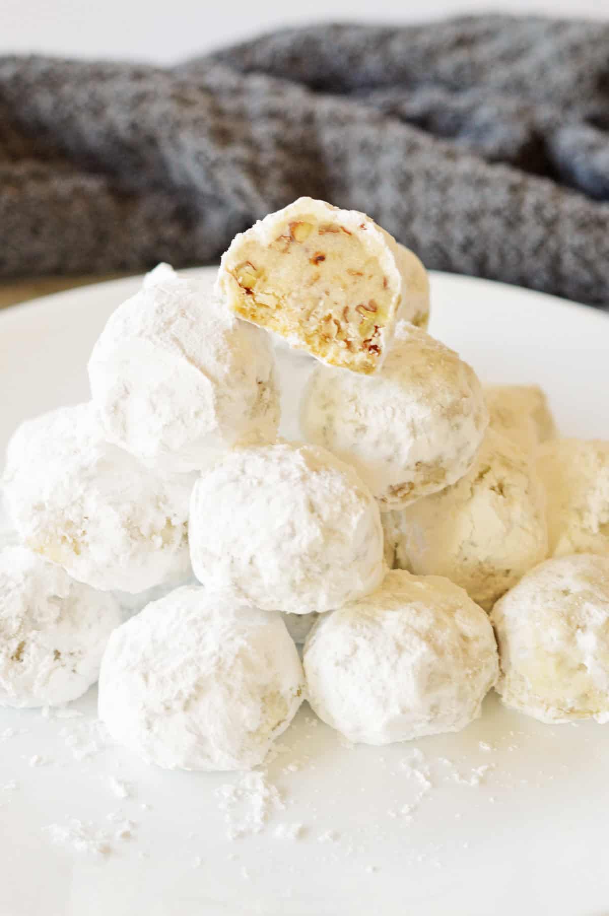 Stack of buttery pecan snowballs with top cookie cut in half to show pecan stuffed inside.