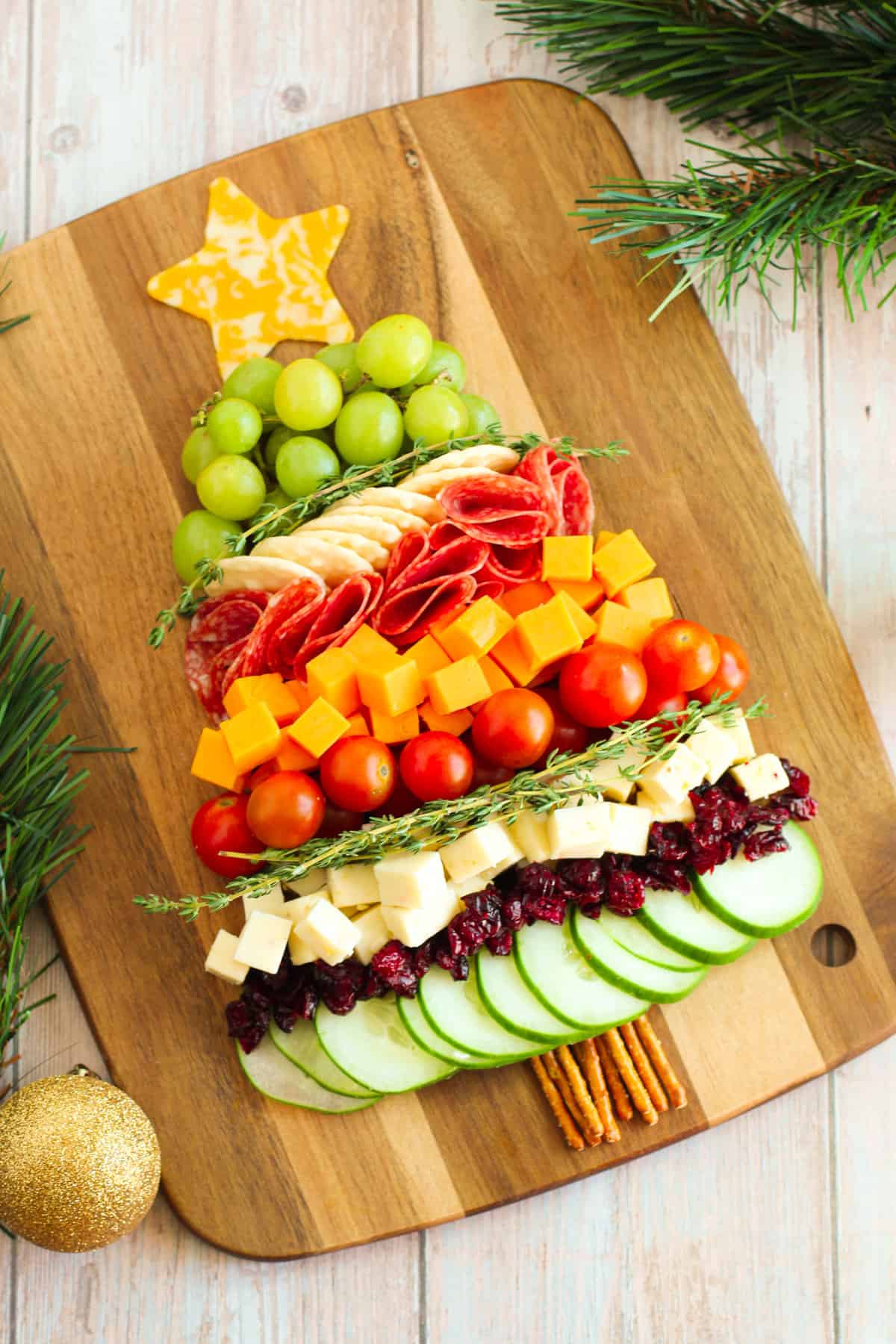 Charcuterie board shaped like a Christmas tree with cheese, cucumbers, tomatoes, grapes, salami, etc...