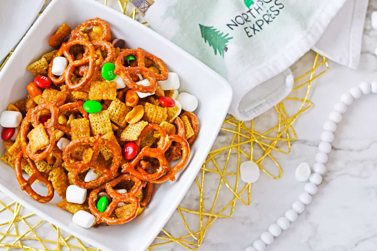 Chex mix with red and green M&M candies in small white bowl.