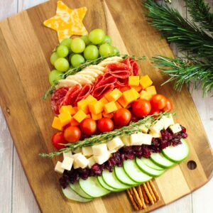 Charcuterie board shaped like a Christmas tree with cheese, cucumbers, tomatoes, grapes, salami, etc...