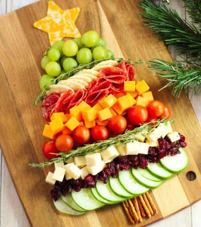 Charcuterie board shaped like a Christmas tree with cheese, cucumbers, tomatoes, grapes, salami, etc...