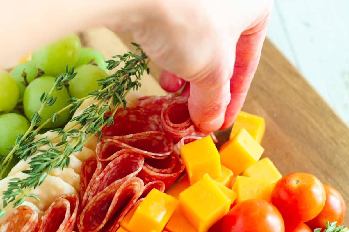 Hand placing salami on board.