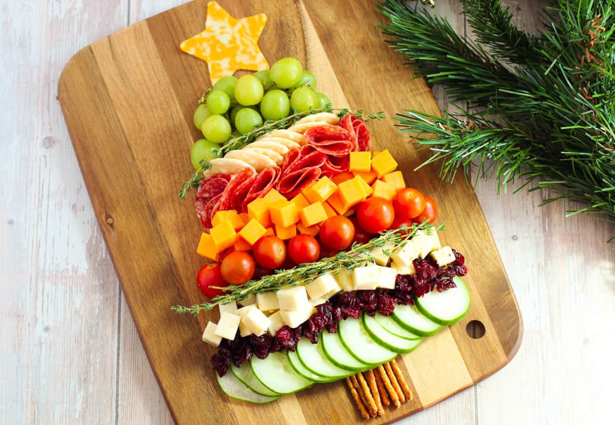 Charcuterie board shaped like a Christmas tree with cheese, cucumbers, tomatoes, grapes, salami, etc...