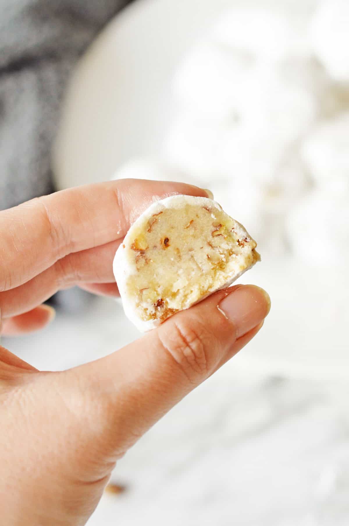 Hand holding snowball cookie with bite taken out of it to show buttery cookie.