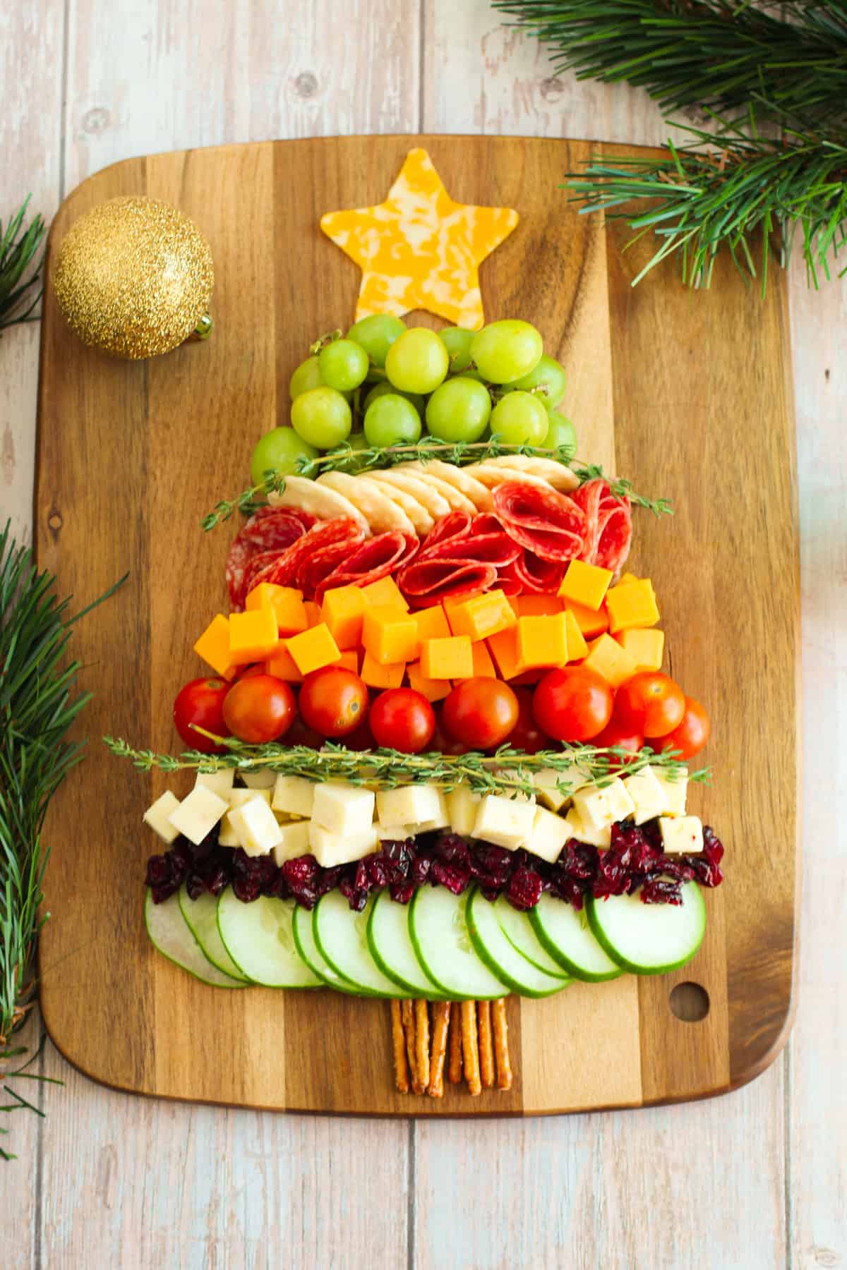 Charcuterie board shaped like a Christmas tree with cheese, cucumbers, tomatoes, grapes, salami, etc...