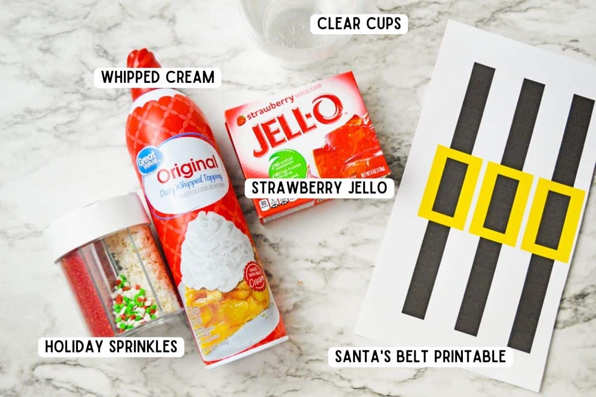 Christmas sprinkles, box of Strawberry jello, can of whipped cream, clear plastic cups, and paper with santa belt designs. 
