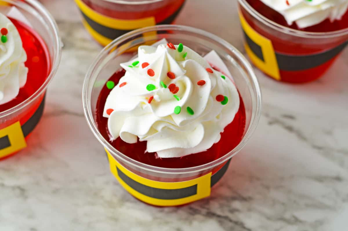 Red jello cup topped with whipped cream and sprinkles.