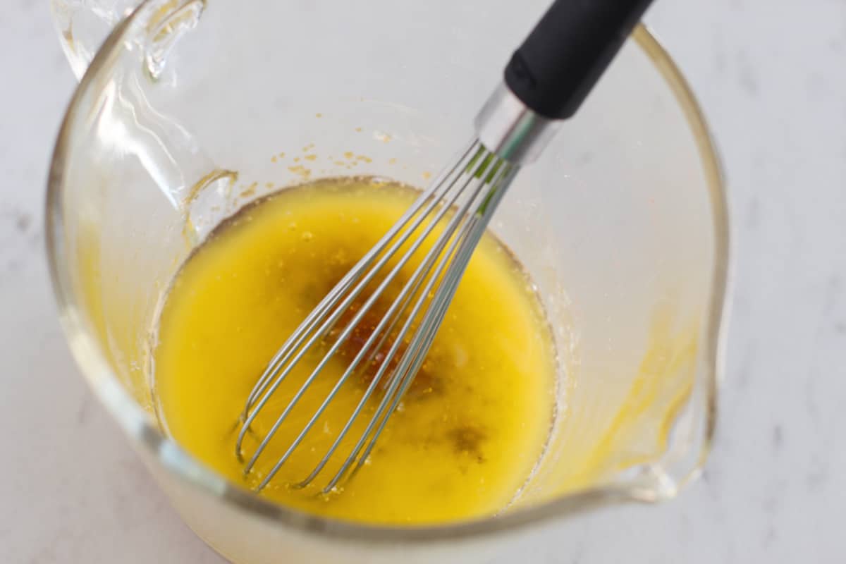 Butter, brown sugar, garlic, and salt being whisked together in glass measuring cup.