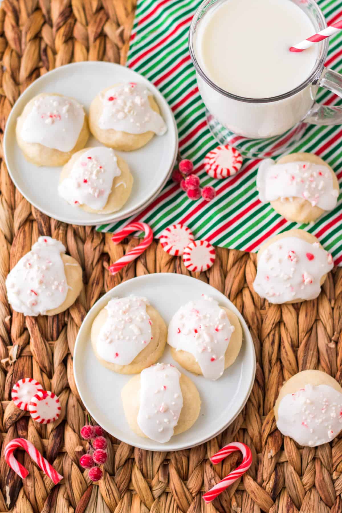 Frosted peppermint cookies on white plates and on straw tray beside a glass of milk.