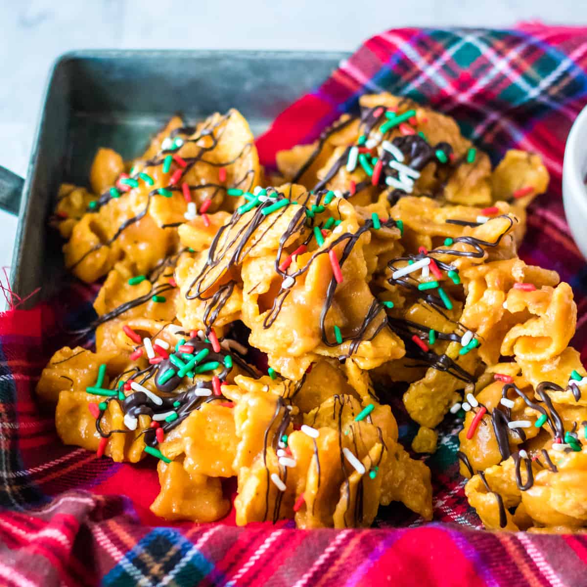 Peanut butter fritos candy topped with a drizzle of chocolate and Christmas sprinkles.