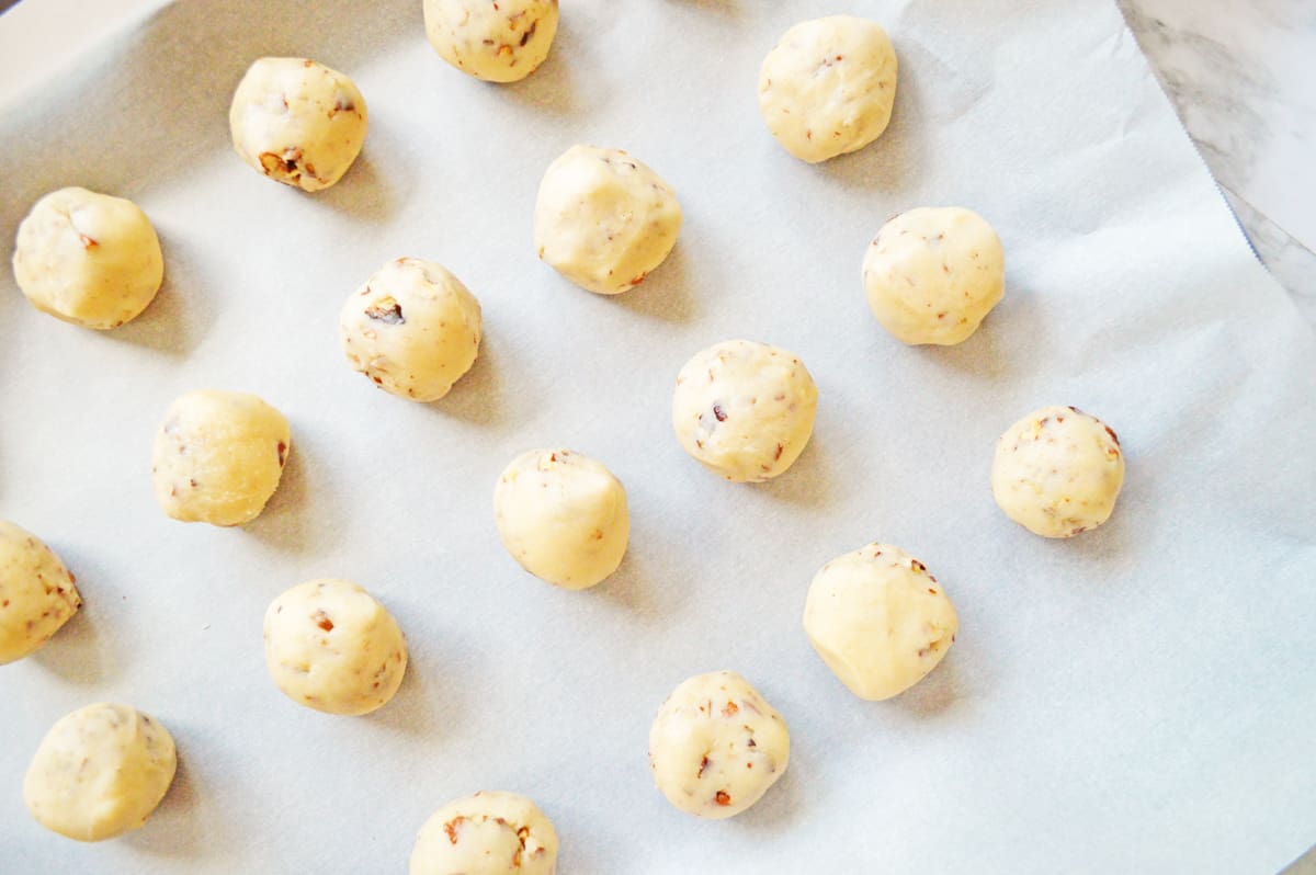 Pecan snowball cookie dough balls on lined baking sheet.