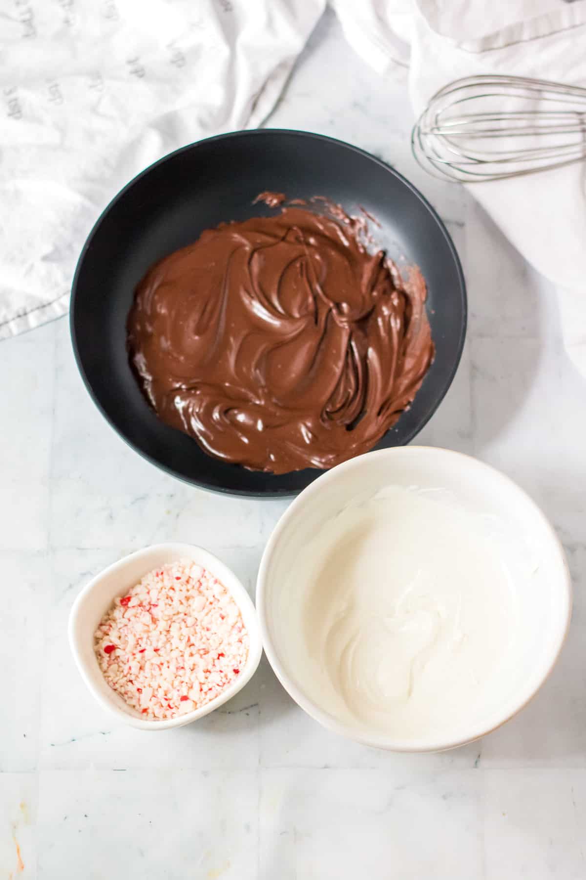 Bowls of melted chocolate, melted white chocolate, and crushed peppermints.
