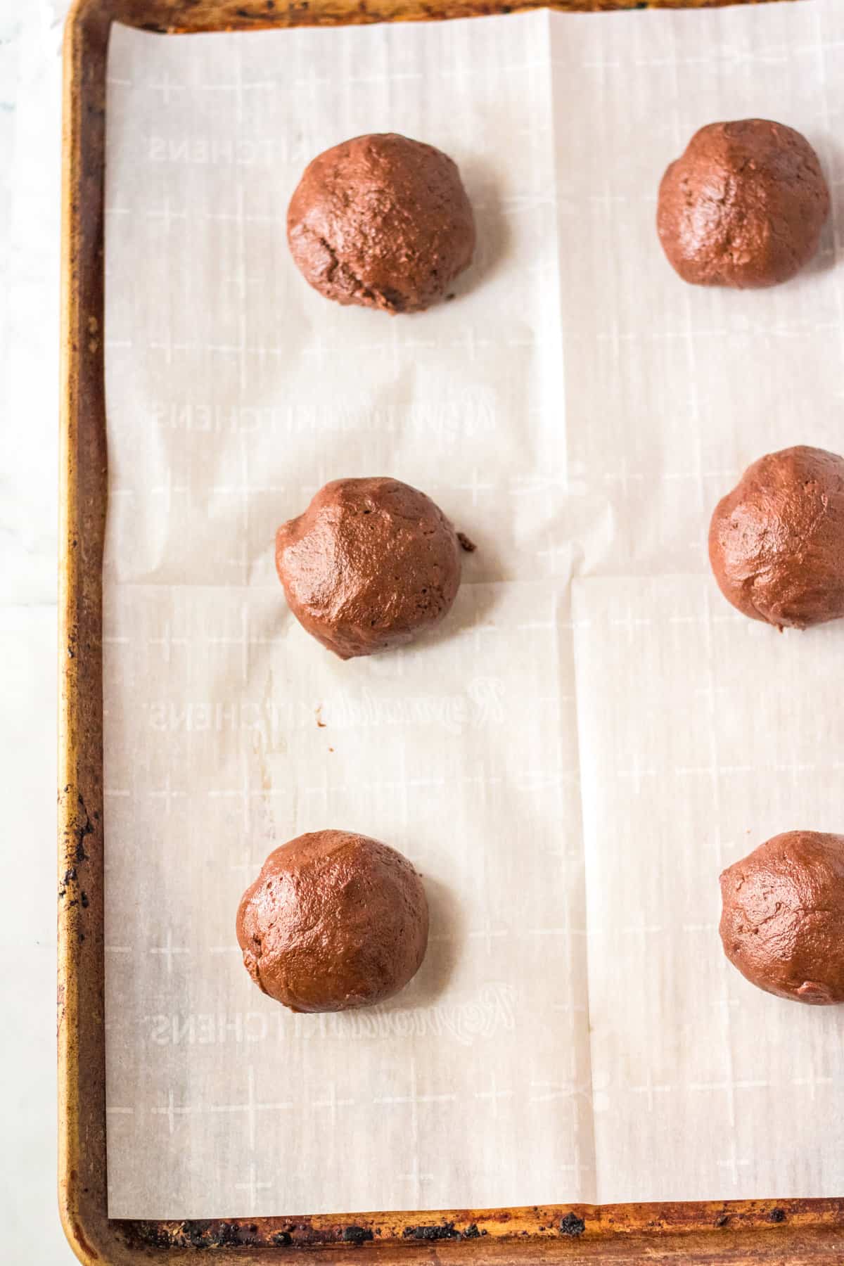 Chocolate cookie dough rolled into large balls on lined cookie sheet.
