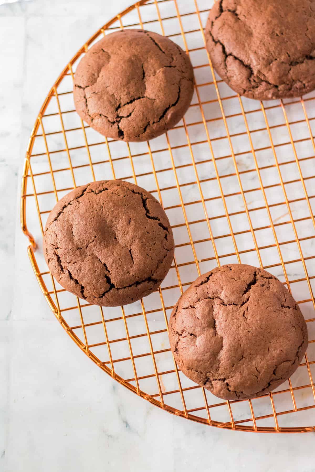 Large, thick chocolate cookies on brass cooling rack.