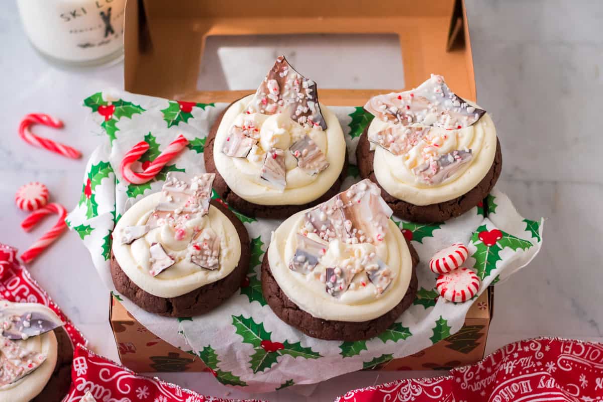 Christmas treat box with holiday napkin and chocolate peppermint cookies topped with frosting and peppermint bark.