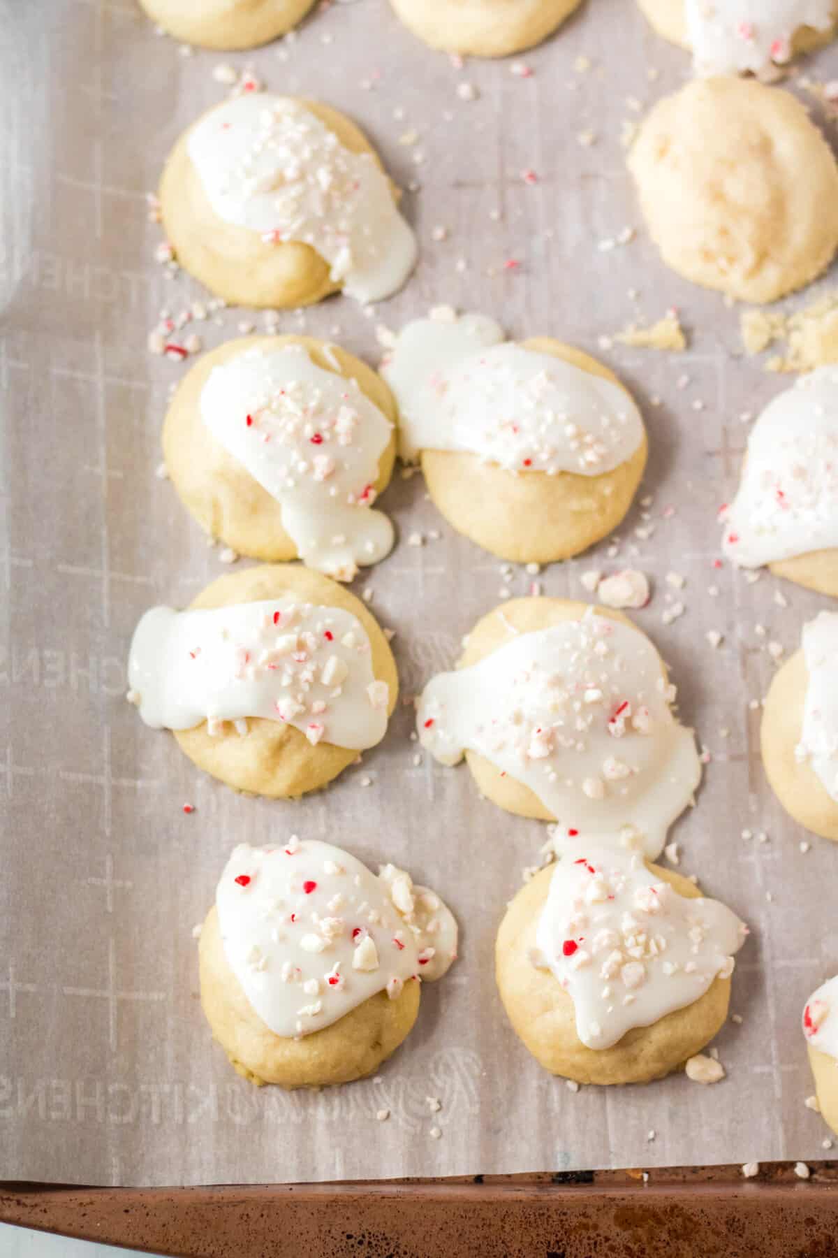 Iced cookies topped with peppermint on lined baking sheet.