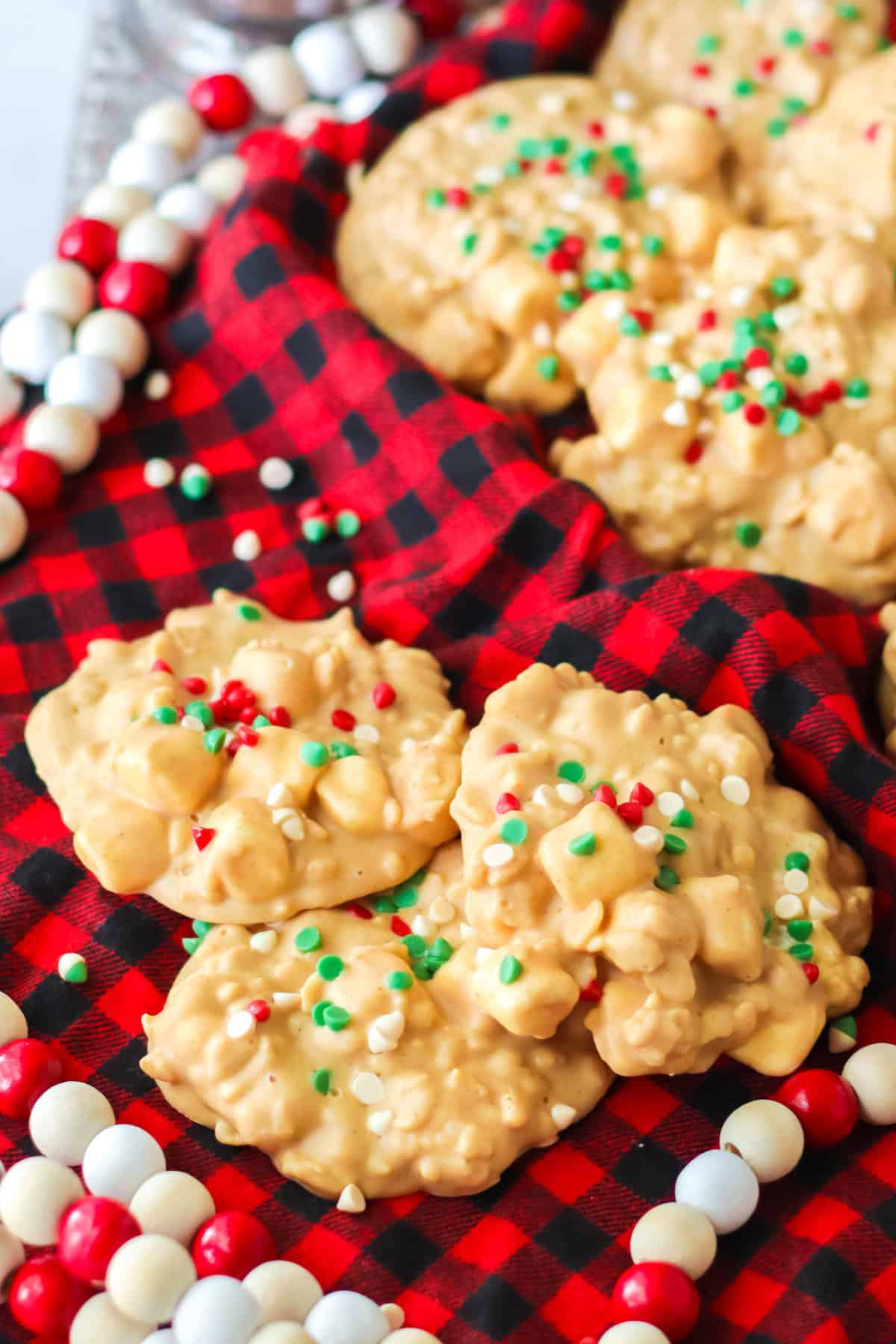 White chocolate, peanut butter, and marshmallow clusters topped with christmas sprinkles surrounded by holiday decor.