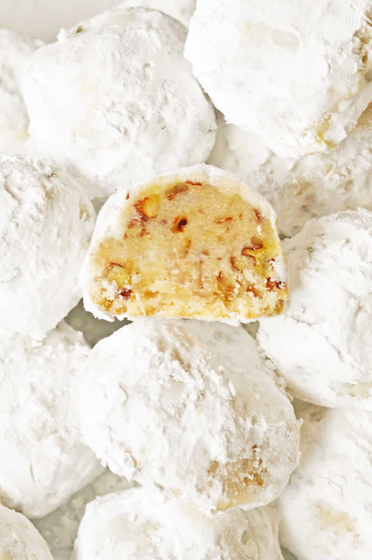 Classic snowball cookies with one cookie halved to show buttery texture and chopped pecans inside.
