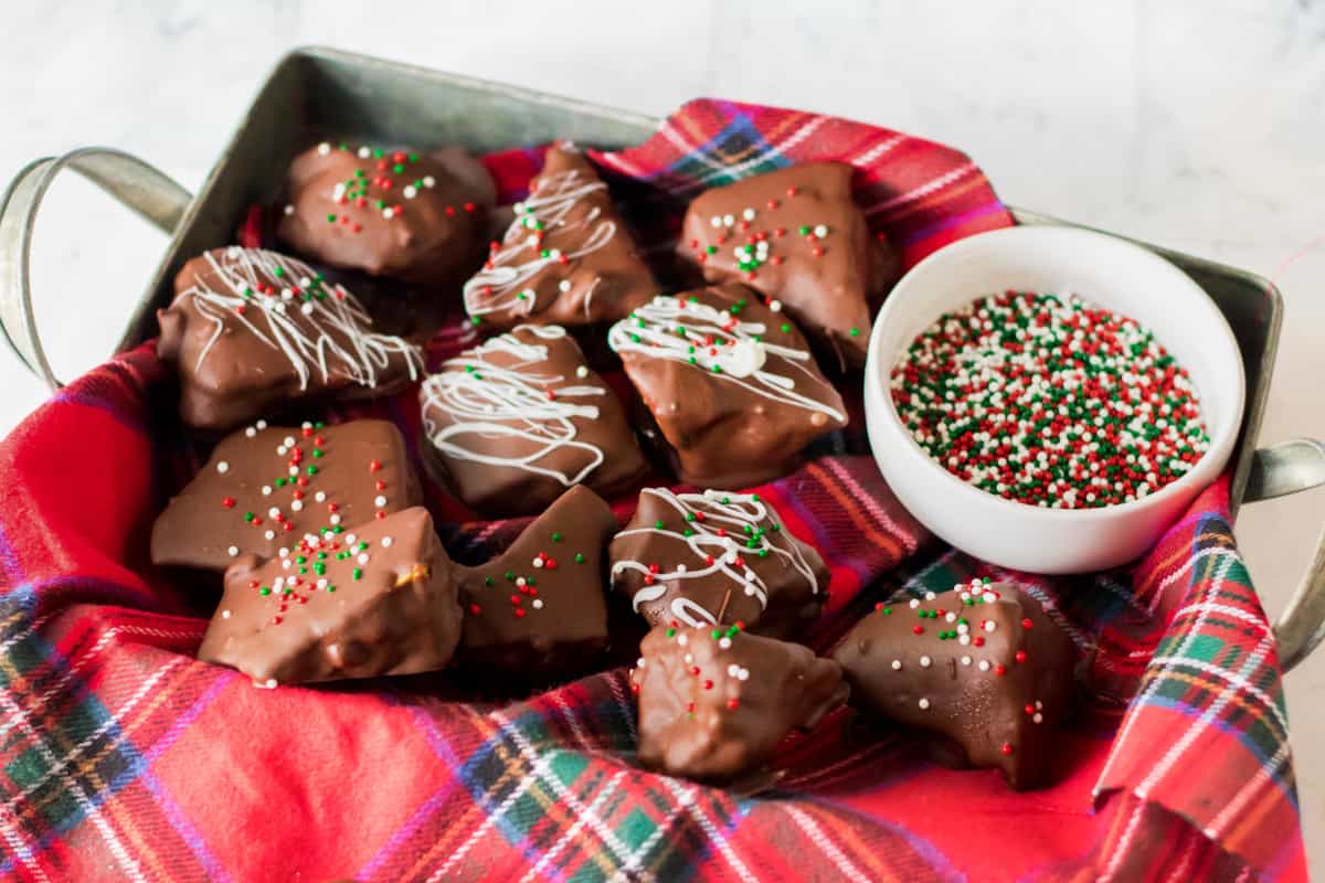 Chocolate coated honeycomb candy in napkin-lined tray with bowl of holiday sprinkles.