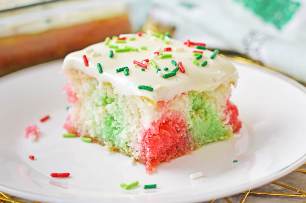 Square slice of jello poke cake with red and green jello injected throughout.