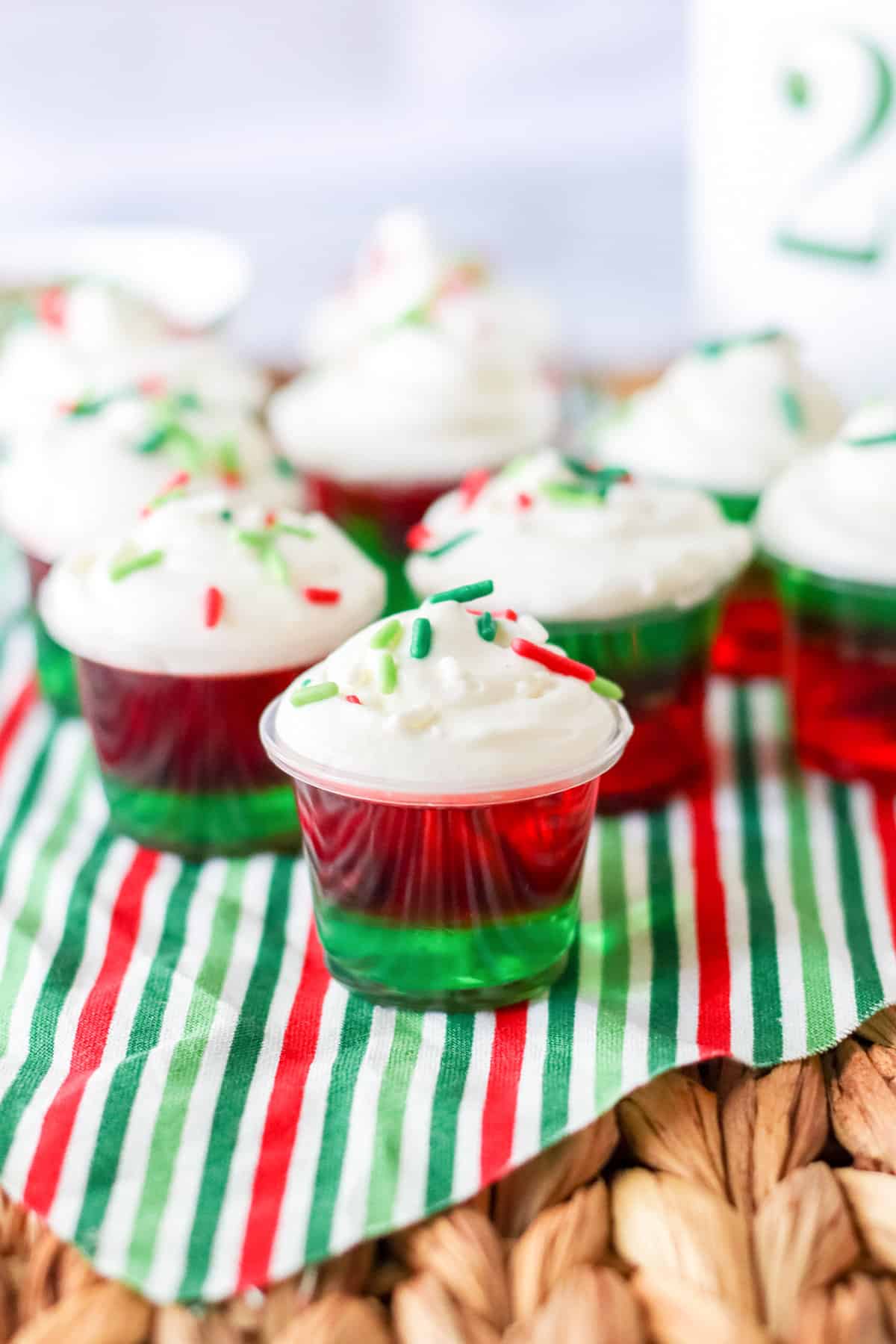 Layered Christmas jello shots topped with whipped cream and sprinkles on red and green striped napkin.