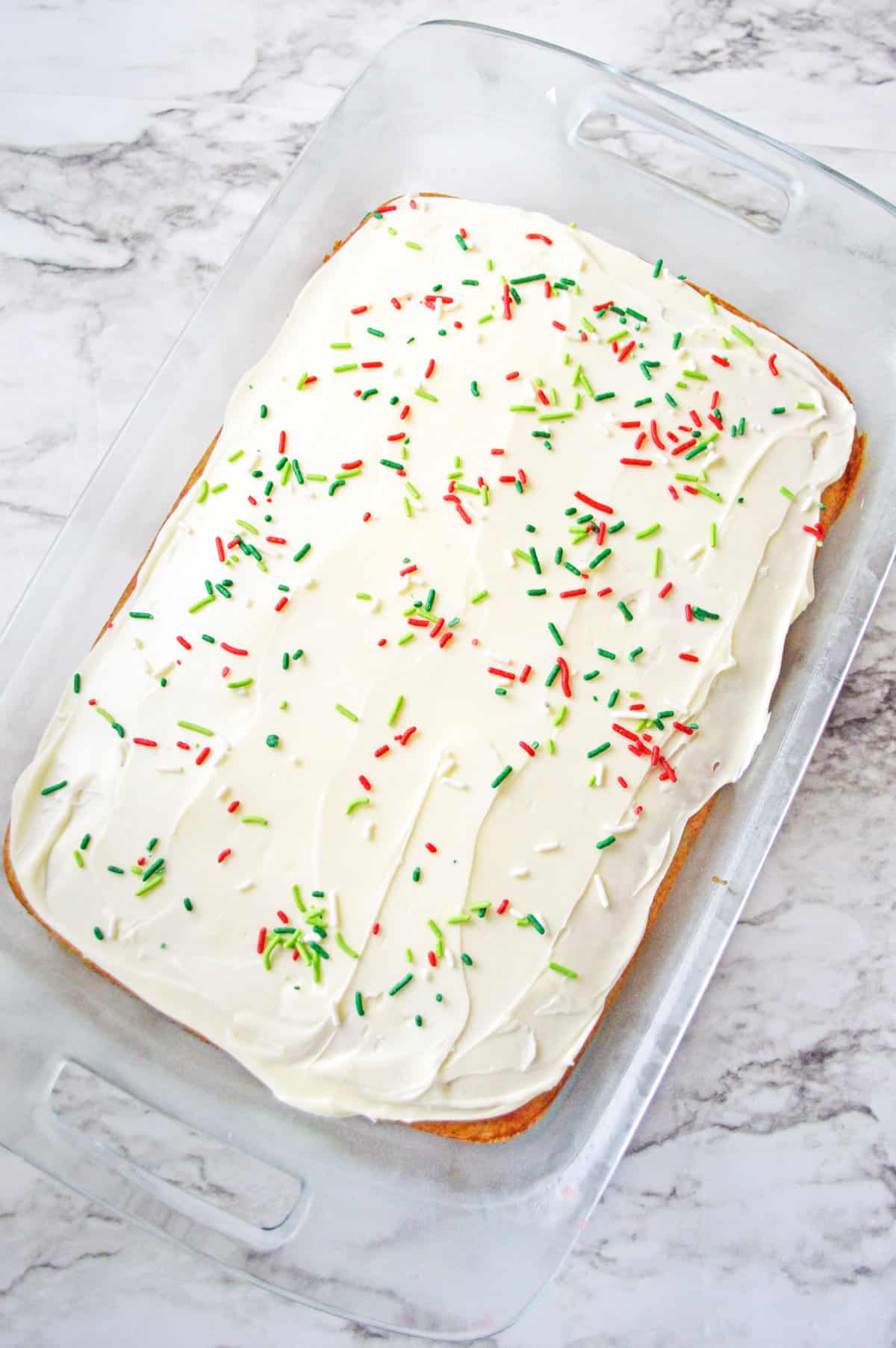 Rectangular cake in 9x13 baking dish topped with vanilla frosting and christmas sprinkles.