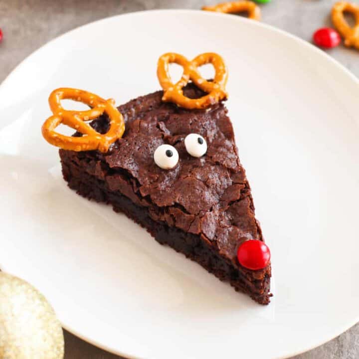 Chocolate brownie decorated like an adorable reindeer with pretzel twist antlers, red M&M nose, and candy eyes.
