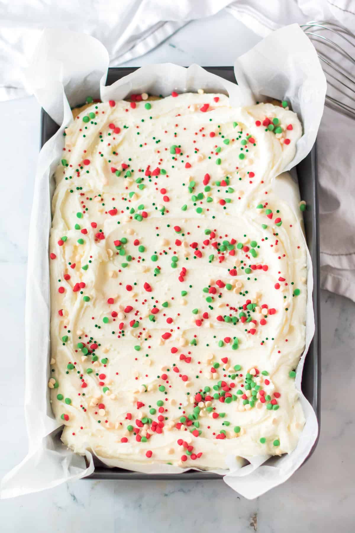 Pan of Holiday cookie bars topped with vanilla buttercream, holiday chips, and sprinkles.