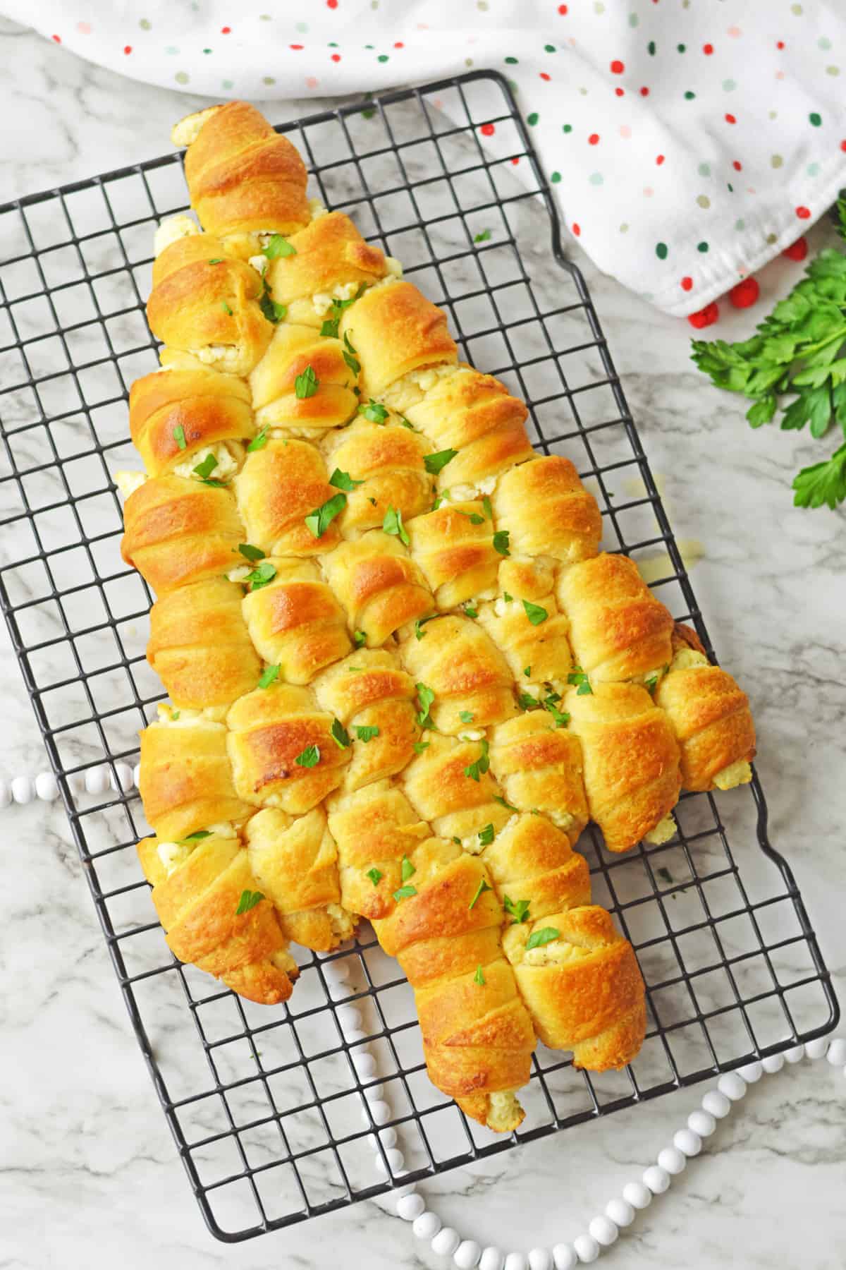 Pull-apart crescent roll Christmas Tree topped with melted butter and parsley on wire rack.