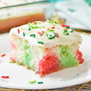 Christmas poke cake with pockets of red and green color throughout a fluffy white sheet cake and vanilla frosting with red and green sprinkles.