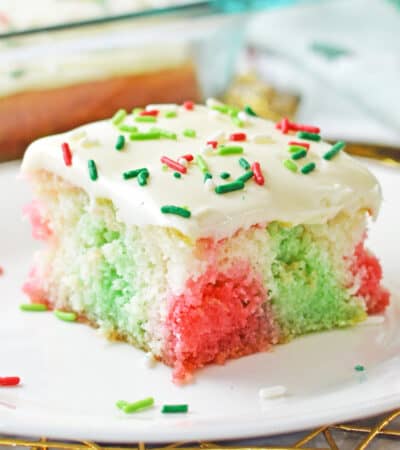 Christmas poke cake with pockets of red and green color throughout a fluffy white sheet cake and vanilla frosting with red and green sprinkles.