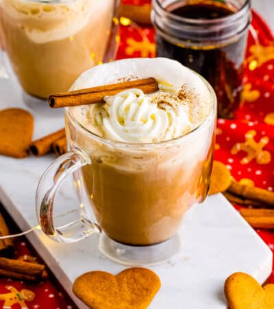 Homemade gingerbread latte in glass mug topped with whipped cream and a cinnamon stick. Heart-shaped gingerbread cookies are next to the hot drink.