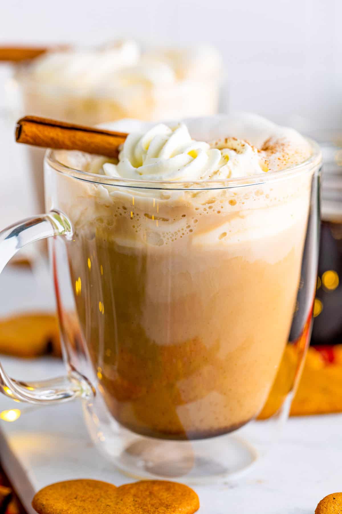 Close up side view of gingerbread spice latte with frothed milk and whipped cream in glass mug.