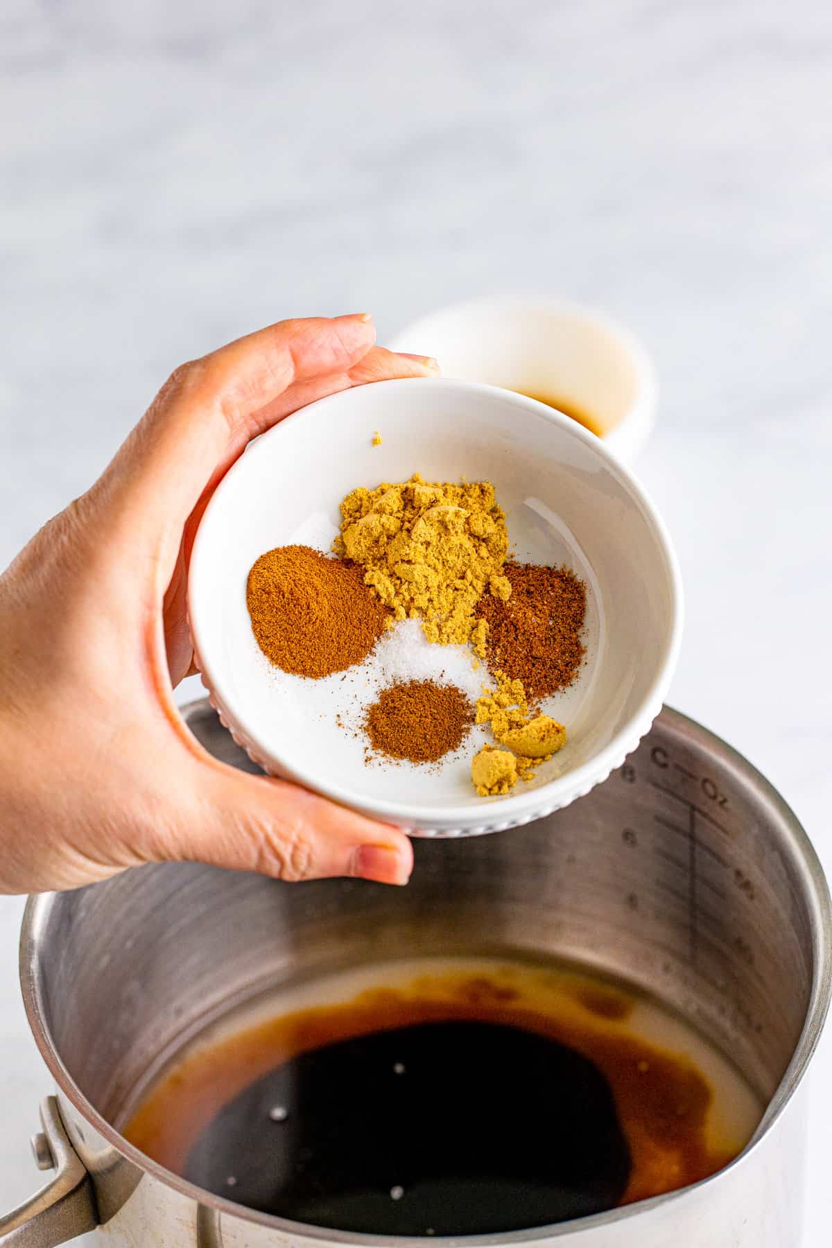 Bowl of spices being added to saucepan.