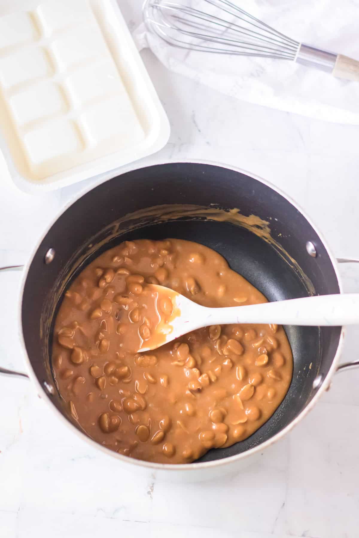 Caramel peanut mixture in saucepan with wooden spoon.