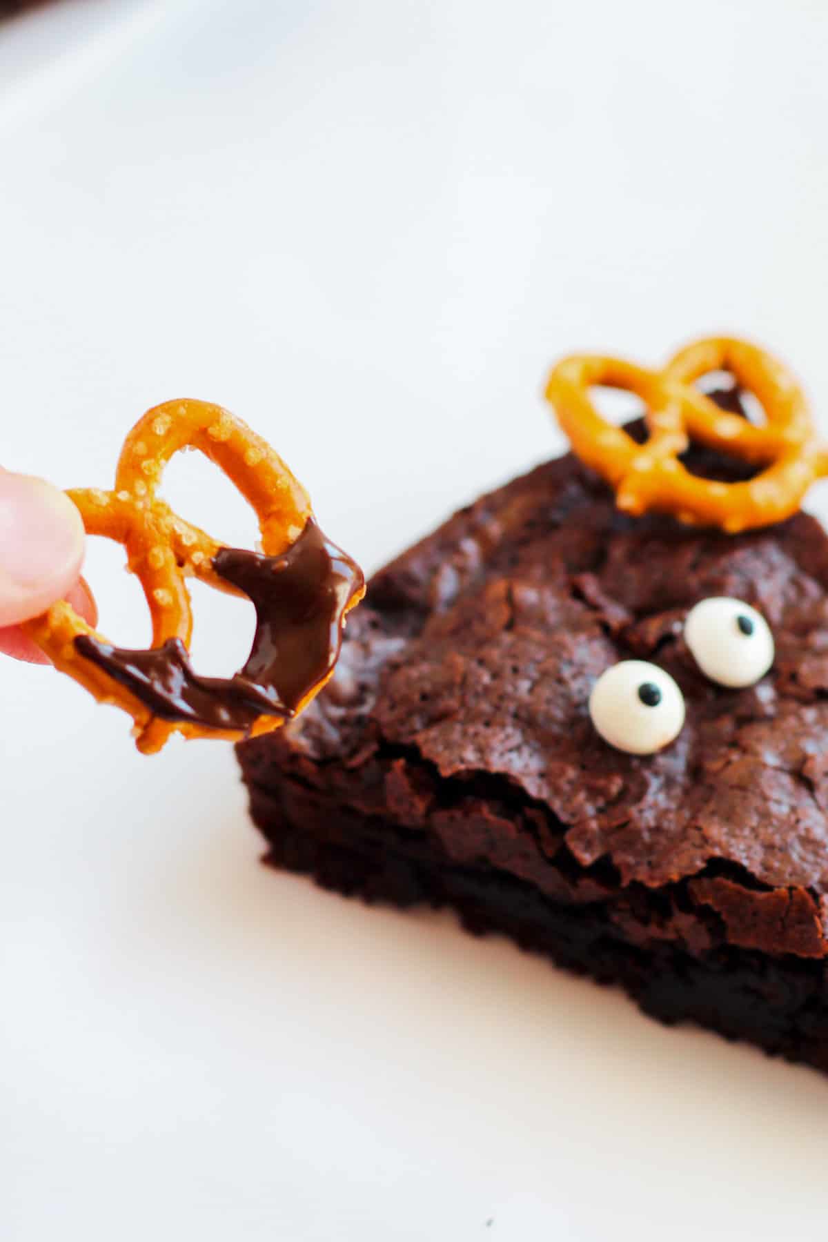 Melted chocolate on pretzel twist, being placed on brownie above eyes.