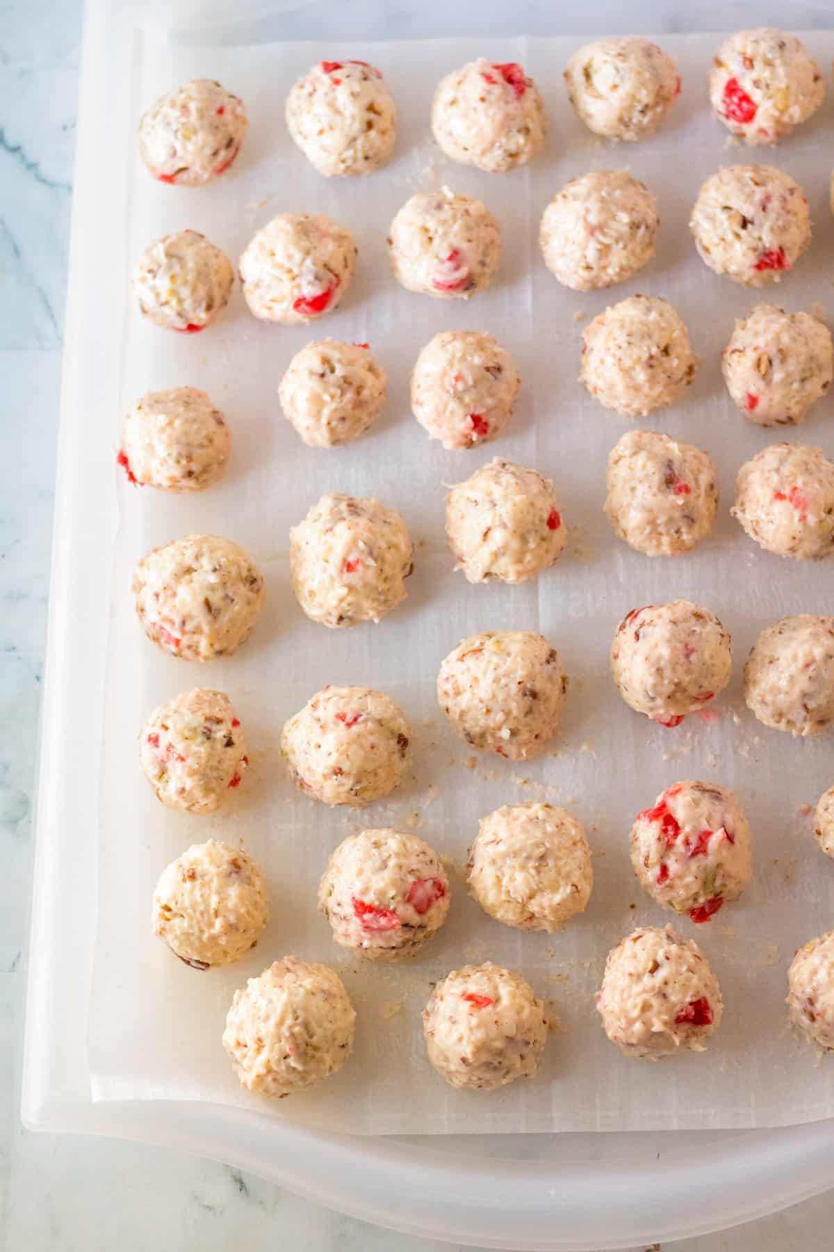 Cherry coconut pecan candy balls on lined baking sheet.