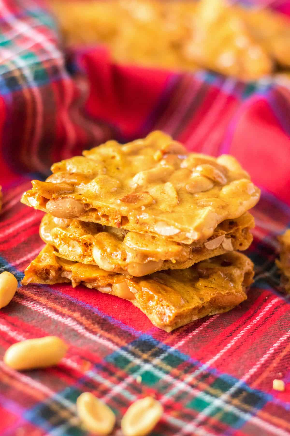Pieces of peanut brittle stacked on top of one another with roasted peanuts sprinkled around them.