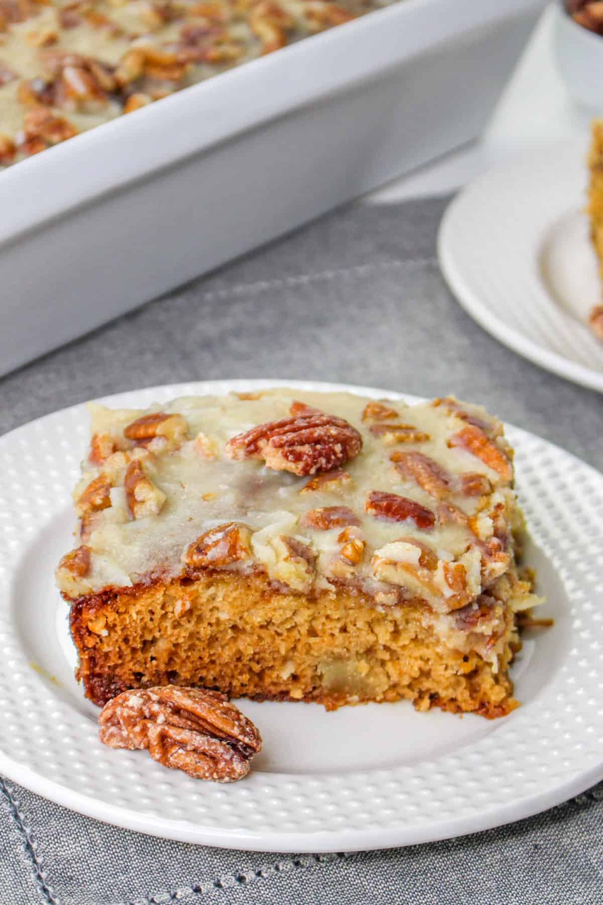 Fruit cocktail cake slice on a white plate with a pecan on top and pecan beside it.