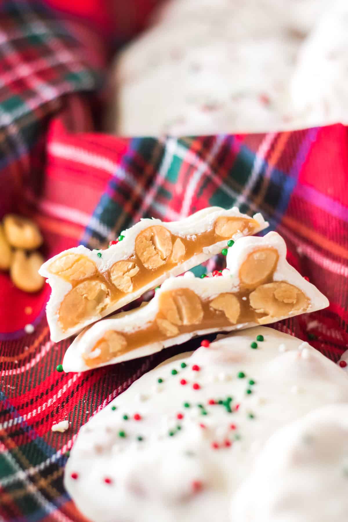 Polar bear paws candy on red plaid cloth. One candy is cut in half to show caramel nut cluster inside.