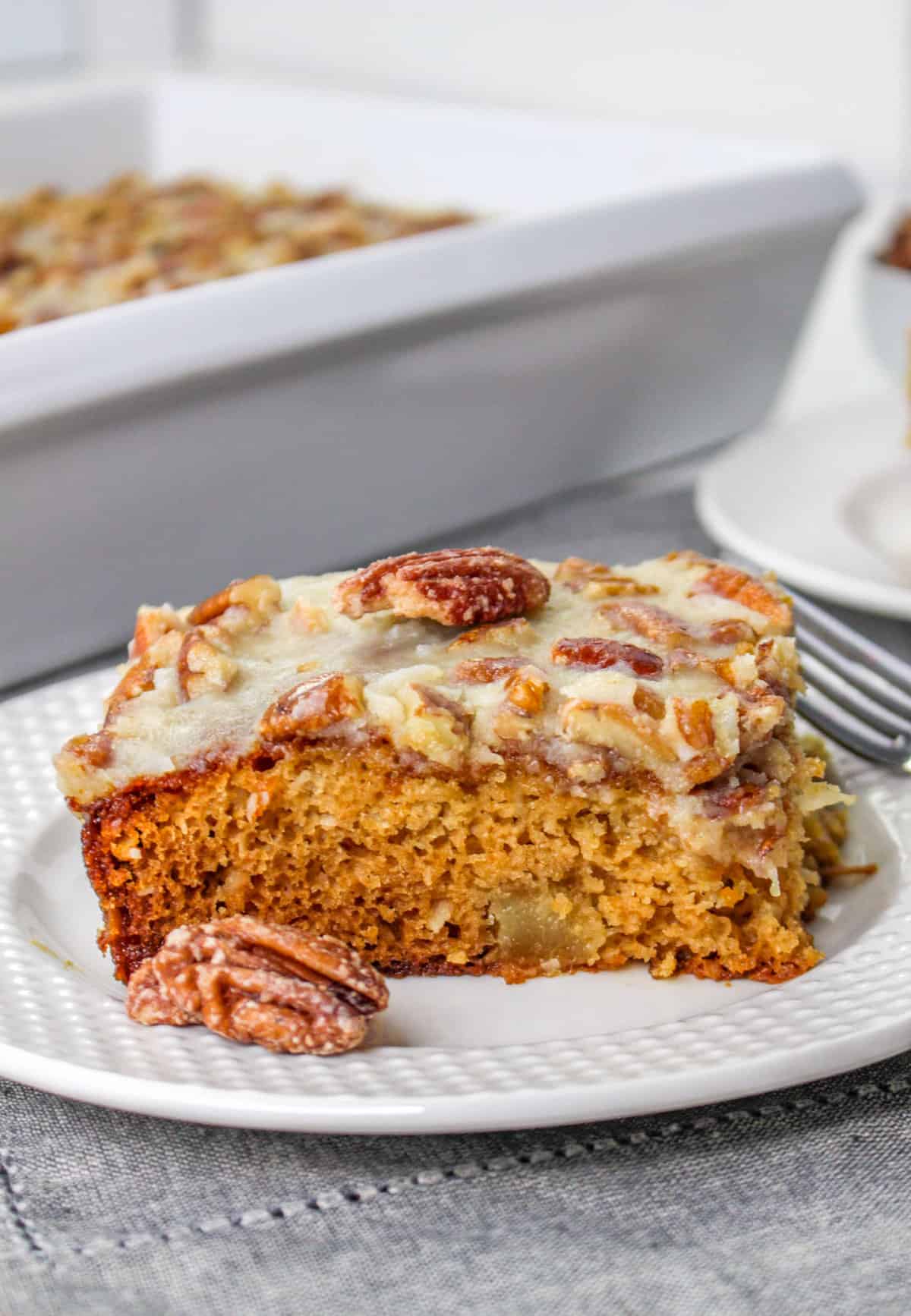 Fruit cocktail cake slice on a white plate with a pecan on top and pecan beside it.