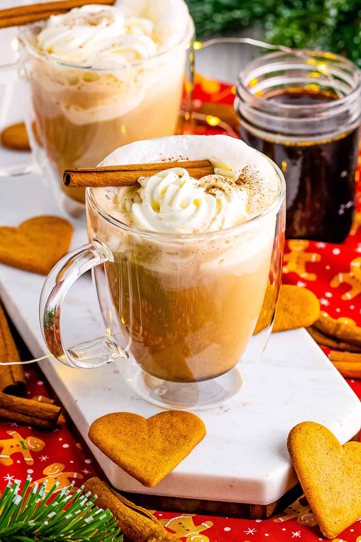 Gingerbread latte surrounded by gingerbread heart cookies, gingerbread syrup in a jar, and Christmas decor.