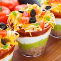 7 layer dip cups with refried beans, guacamole, sour cream, salsa, cheese, olives, green onions, tomatoes, and jalapenos.