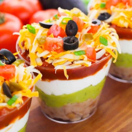 7 layer dip cups with refried beans, guacamole, sour cream, salsa, cheese, olives, green onions, tomatoes, and jalapenos.