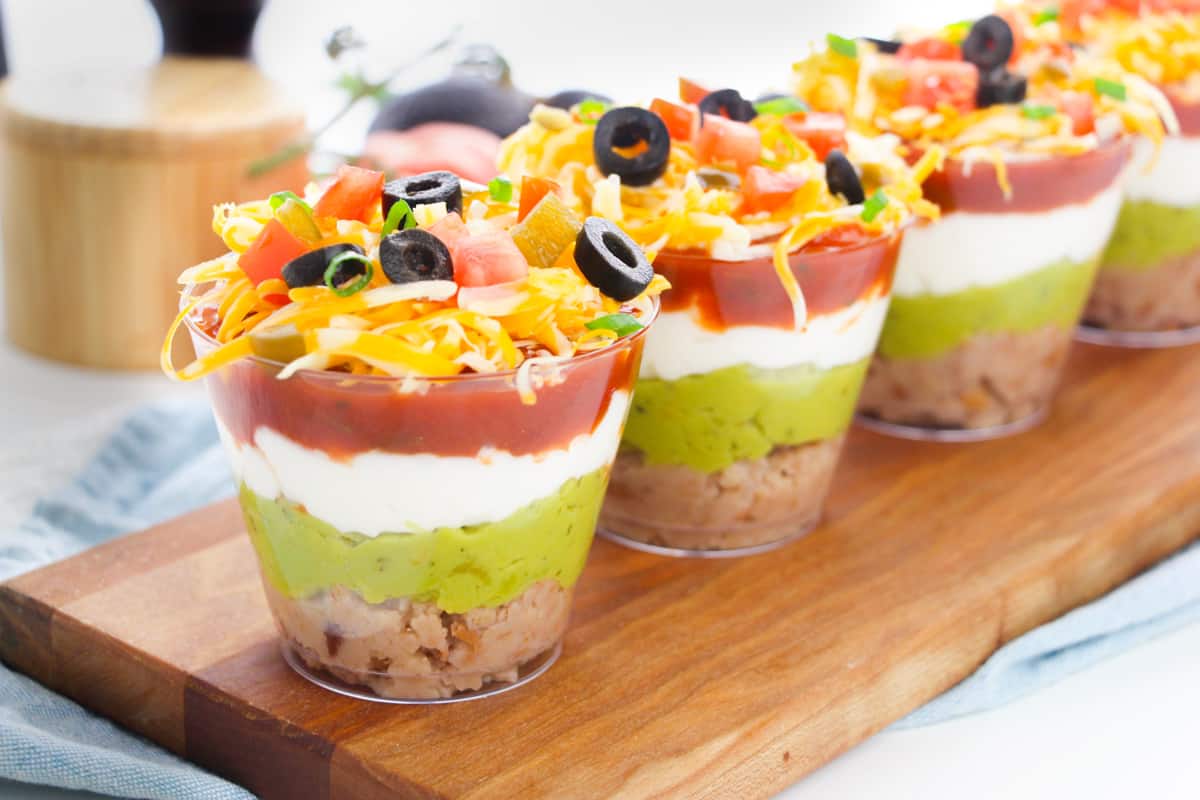 Layered taco dip in individual-sized clear cups.