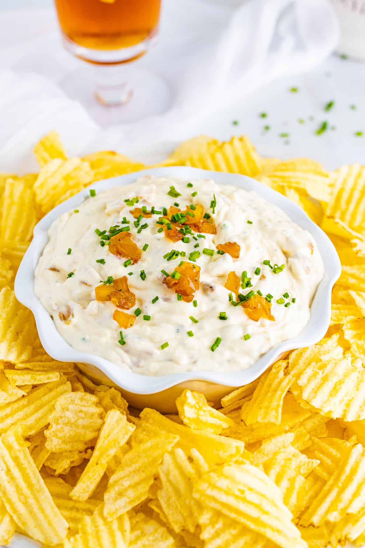 French onion dip garnished with chives in a bowl surrounded by crispy potato chips.