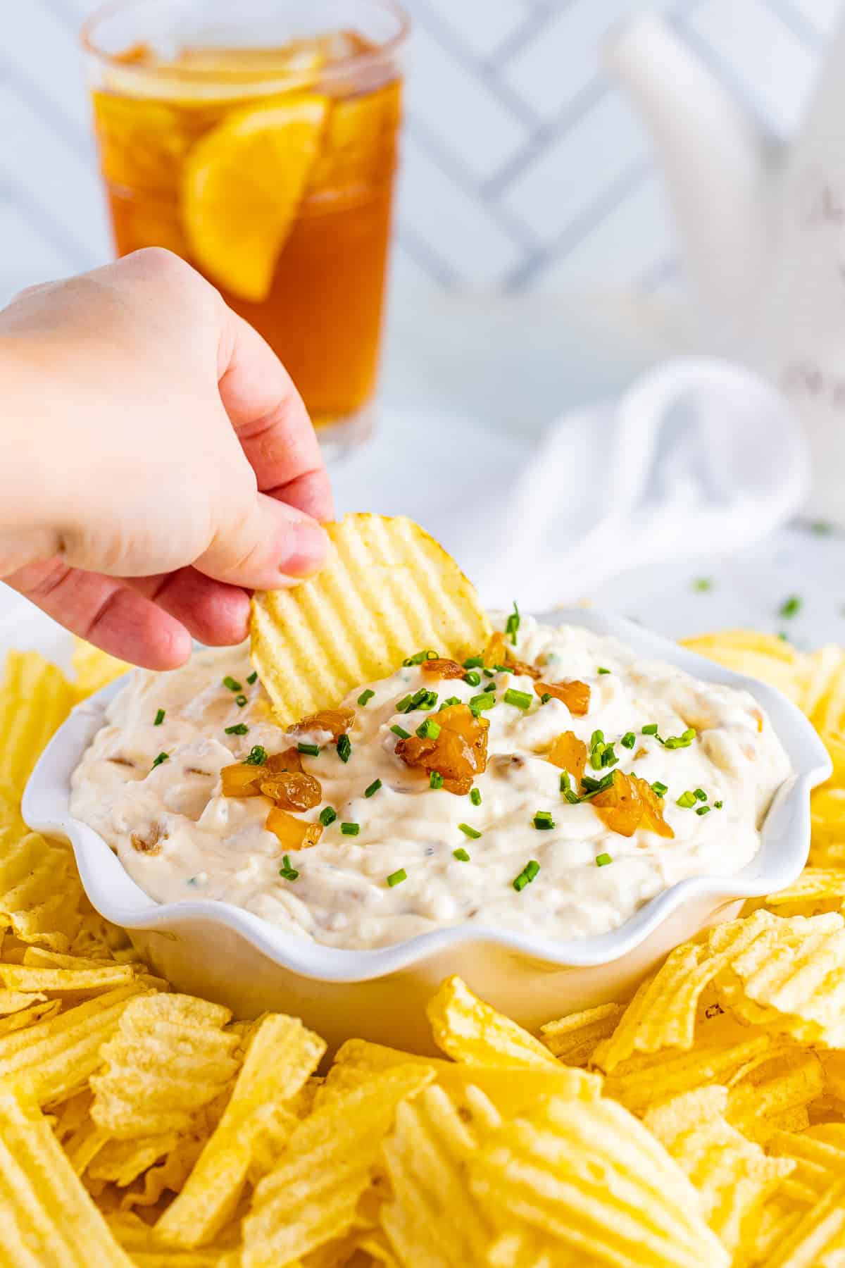 Hand dipping a potato chip in a bowl of French onion dip.