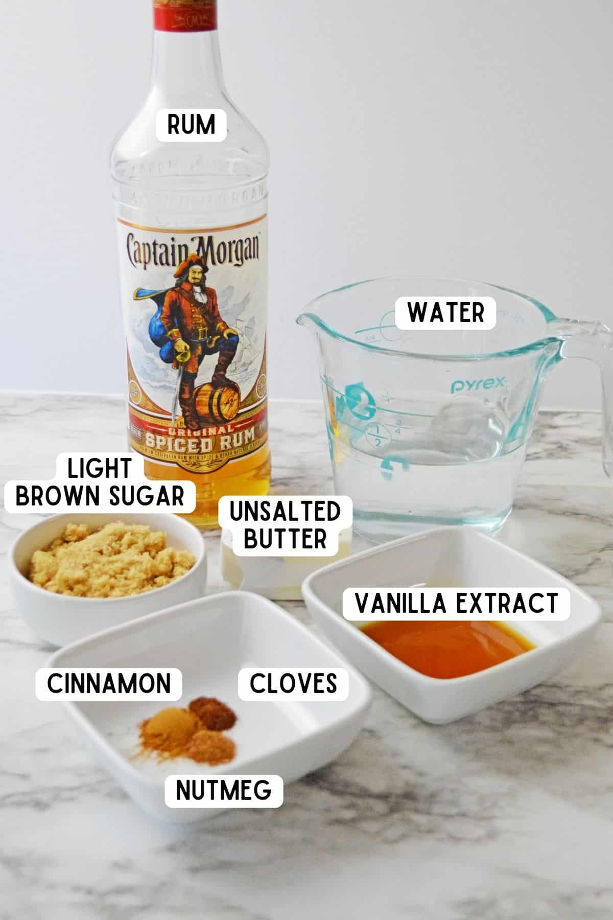 Ingredients for Hot Buttered Rum recipe: bottle of spiced rum, light brown sugar, water, vanilla extract, unsalted butter, cinnamon, cloves, and nutmeg.